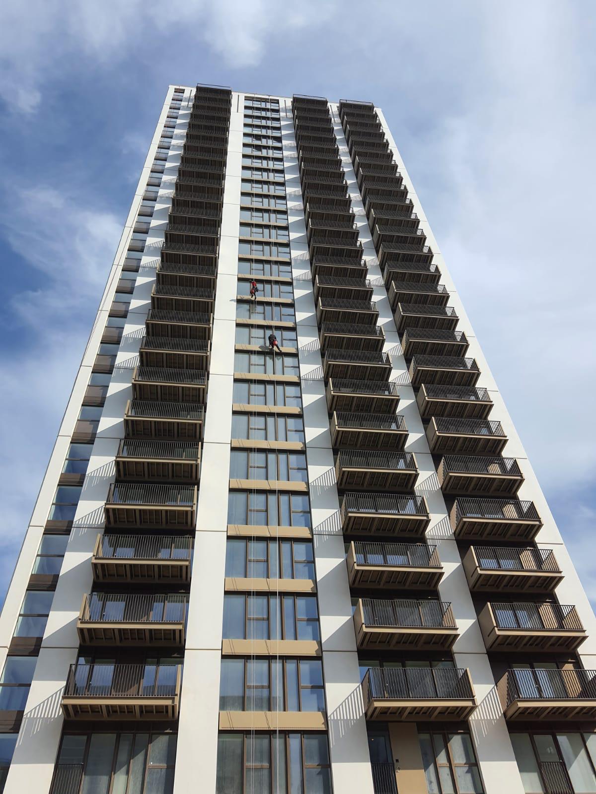 Torre residencial em contrapicado, com dois técnicos em suspensão na fachada