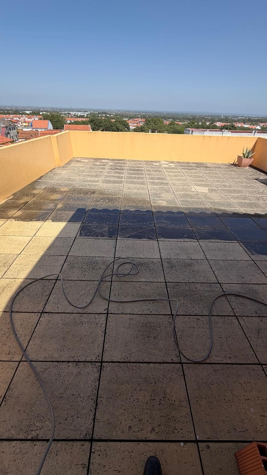 Mangueira sobre o pavimento do terraço durante a lavagem, com a água suja a escorrer