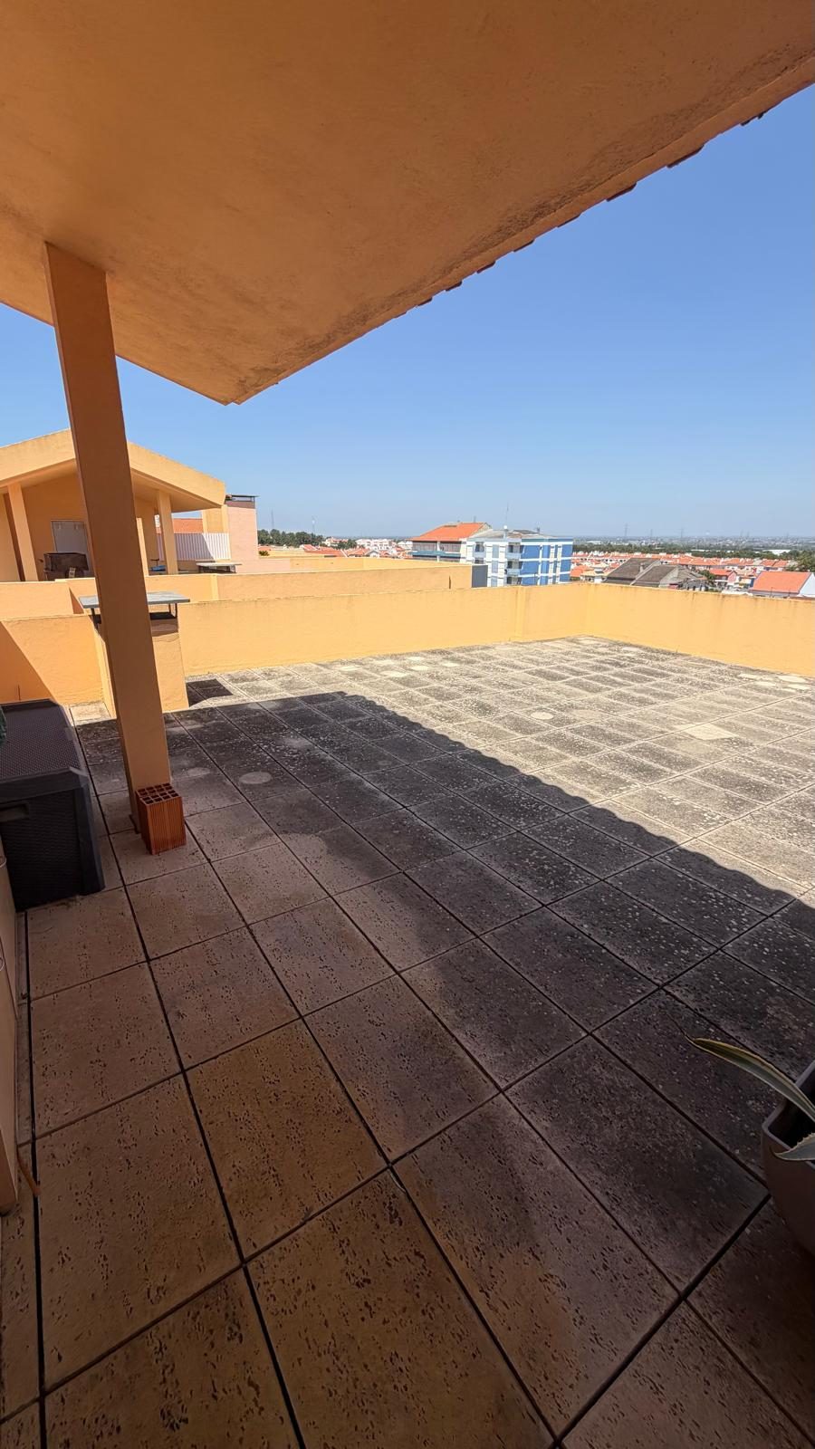 Terraço de cobertura com a lajeta escurecida e depósitos brancos, visto a partir da zona coberta