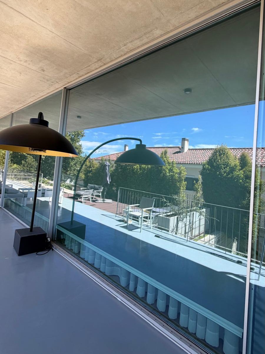 Pano de vidro de correr ao longo de um terraço, a refletir a piscina e a sebe sem marcas